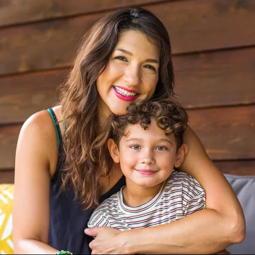 Smiling mother hugging her young son with curly hair in a cozy wooden indoor setting