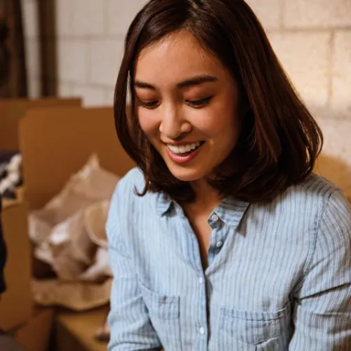 Smiling young woman and man sit near cardboard boxes surrounded by packing materials in a cozy room
