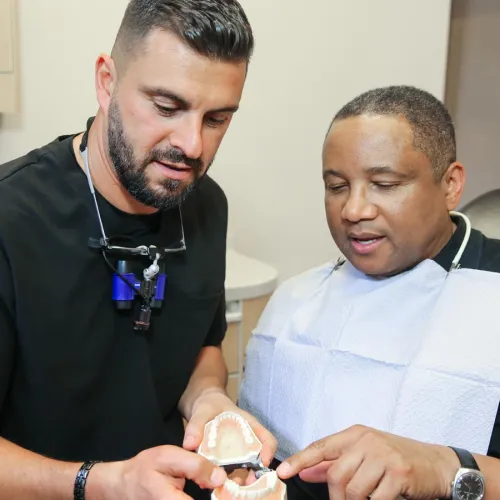 Two dental professionals discuss a dental model in a clinic setting.