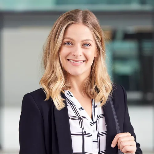 Smiling professional woman in a black blazer inside a modern office space.