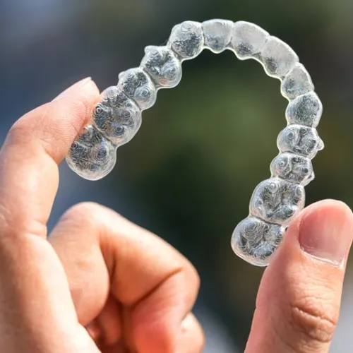 Hand holding a clear dental aligner used for orthodontic teeth straightening against a blurred background