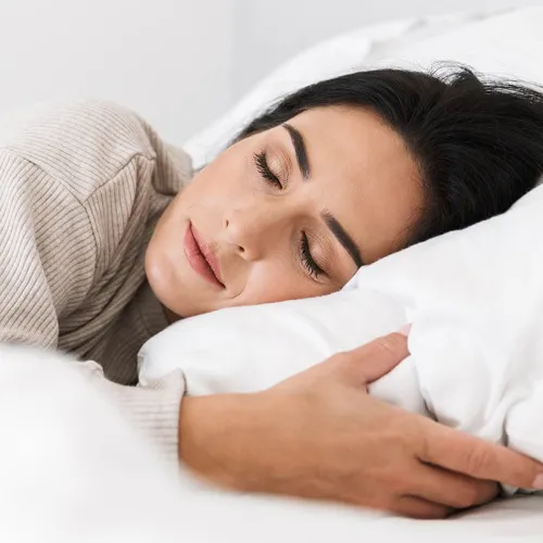 Peaceful woman sleeping on white pillow with cozy beige sweater relaxing in bed.