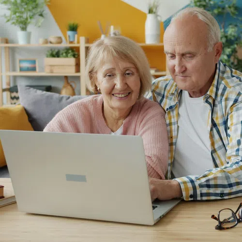 Senior couple smiling and using laptop together at home with cozy decor and plants on table