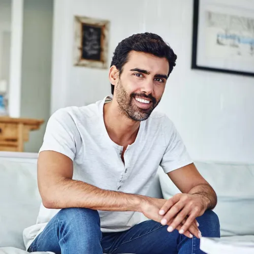 Smiling man in casual attire sitting comfortably on a sofa, exuding warmth and approachability.
