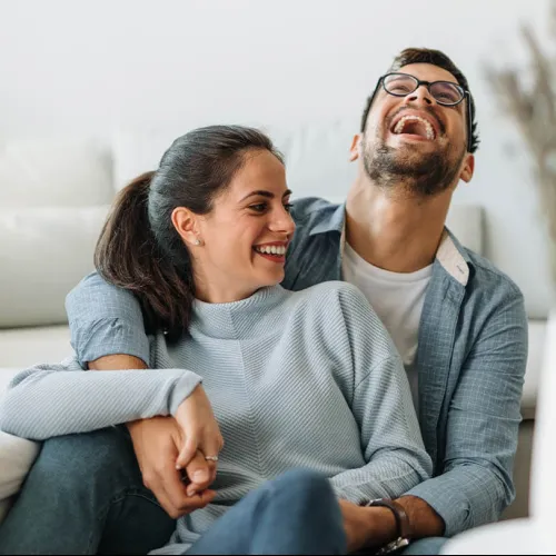 Couple sitting on couch laughing and holding hands in a cozy bright living room setting