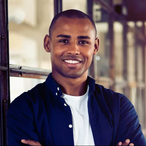 Confident young man smiling with arms crossed wearing a navy shirt and white t-shirt indoors