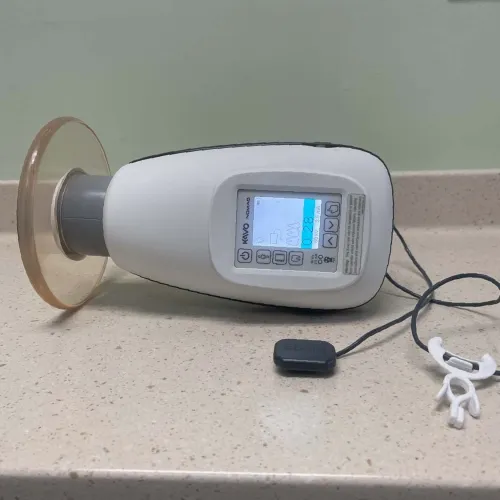Handheld dental device with display screen and wrist strap on beige countertop against green wall.