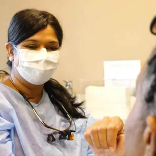 A healthcare professional wearing a mask consults with a patient in a clinical setting.
