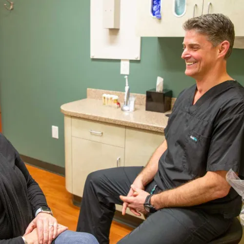 Smiling female patient and male healthcare professional in black scrubs talking in a medical office with green walls.