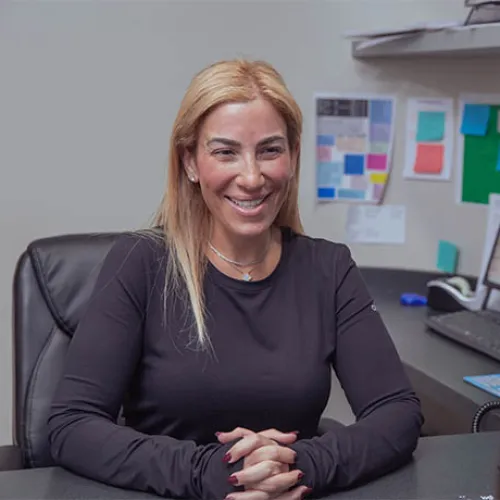 Smiling woman in black shirt sitting at office desk during a conversation with a colleague.