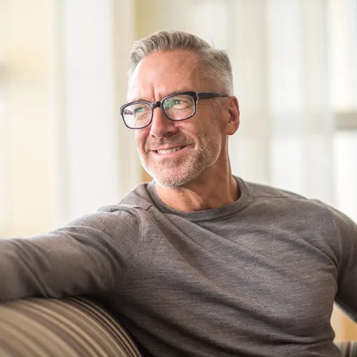 Smiling mature man with glasses relaxing at home, showcasing a cozy indoor atmosphere.