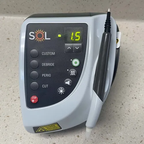 SOL dental laser device with control panel showing power setting 1.5 and attached handpiece on a speckled countertop.