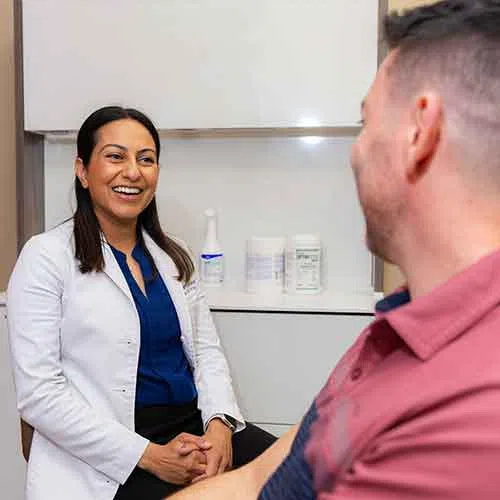 Female doctor smiling and talking with a male patient in a medical office setting.