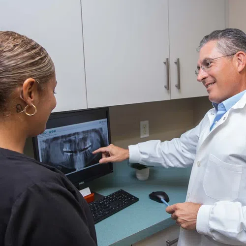 Dentist in white coat reviewing dental x-ray on computer with patient in dental office consultation