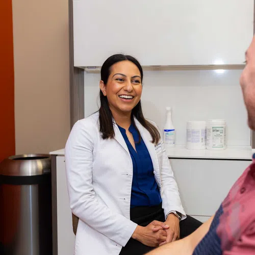 Female doctor smiling and talking with a male patient in a medical office setting.