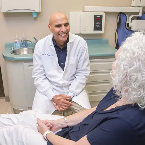 Smiling male dentist in white coat talking with female patient in dental office during consultation