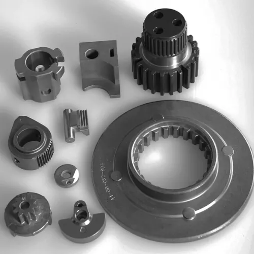 Various small metal industrial machine parts including gears and fittings on a white surface