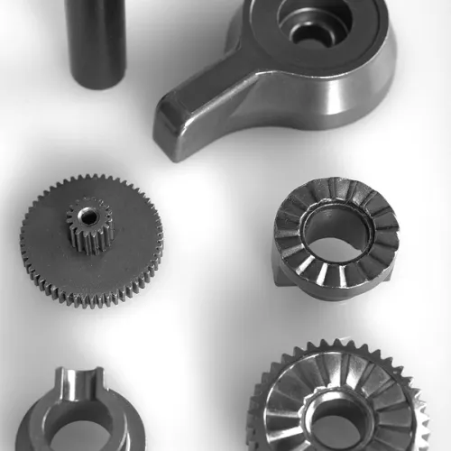Collection of various metal mechanical gears and parts arranged on a white surface in grayscale.
