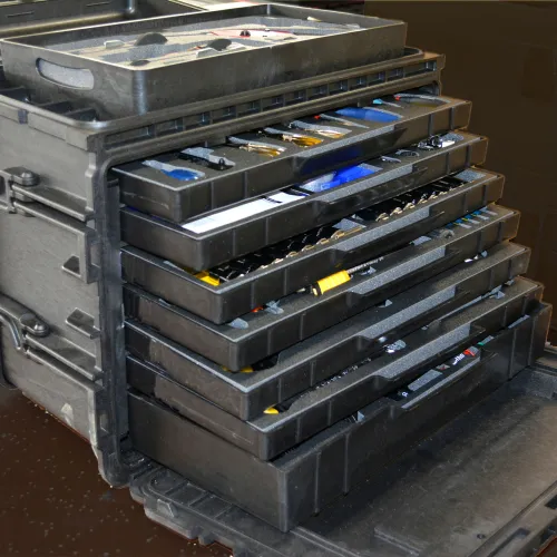 Stack of black plastic trays with tool compartments inside a carrying case, partially open showing organized tools.