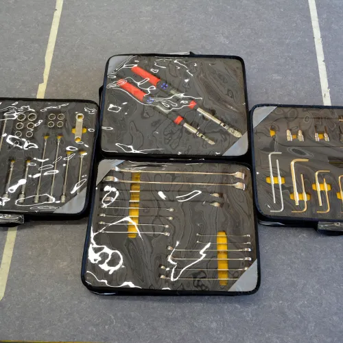 Four black toolkits with transparent covers containing various precision tools on a gray surface.