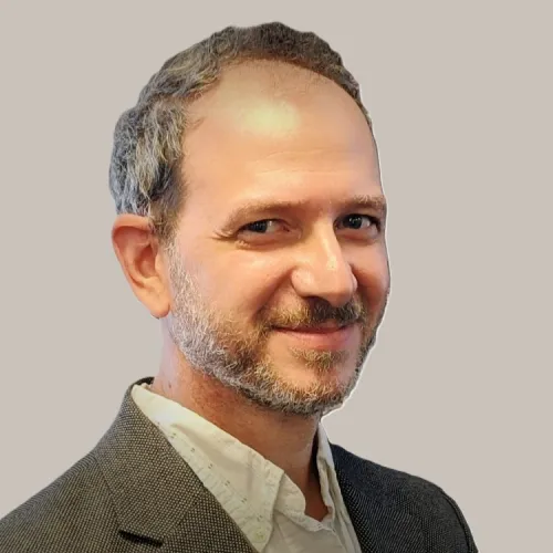 Smiling middle-aged man with grayish beard and short hair wearing a blazer and white shirt