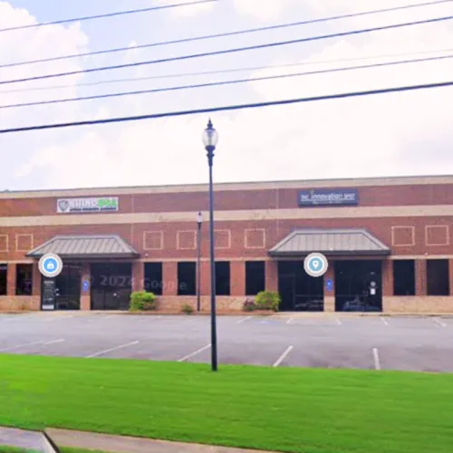 Two-unit brick commercial building with signs for Hibbs PSA and The Innovation Spot, empty parking lot, green lawn.