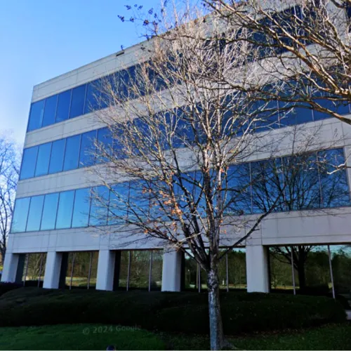 Modern office building with large reflective windows and bare trees in front on a clear sunny day