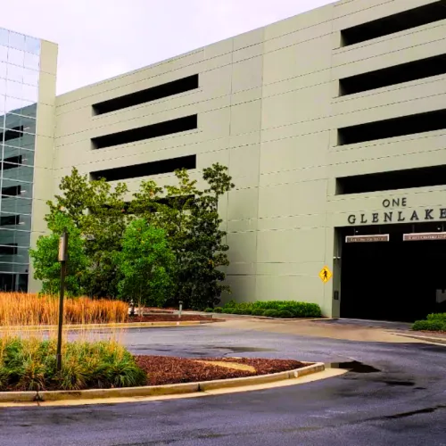 Exterior view of One Glenlake parking garage and modern office building with landscaped greenery around the entrance.