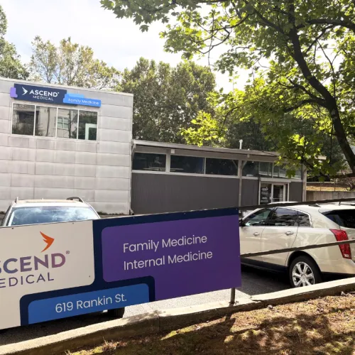 Ascend Medical family and internal medicine clinic with sign and parked cars outside under trees.
