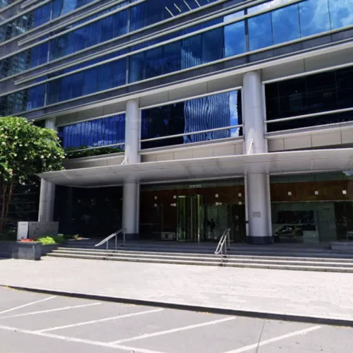 Modern office building entrance with glass facade, wide steps, and a covered awning under blue sky.