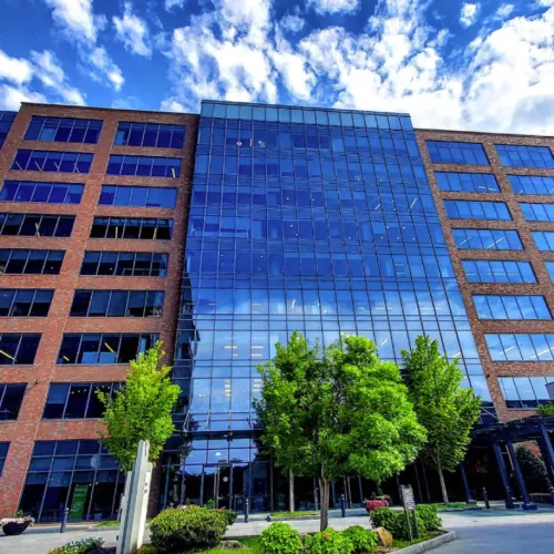 Modern office building with glass facade and brick exterior under a bright blue sky with scattered clouds.