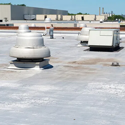 Flat commercial roof with HVAC units and ventilation fans under clear blue sky on a sunny day