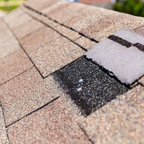 Close-up of asphalt roof shingles with one damaged and partially missing, showing roof repair needs.