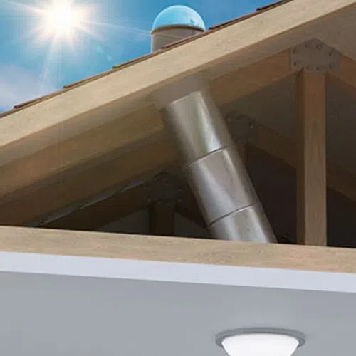 Metal exhaust pipe installed through wooden roof structure with sun flare and ceiling light below
