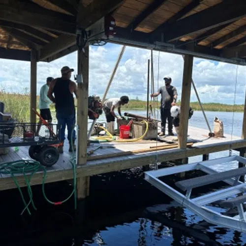 Group of people working on a wooden dock over a lake with equipment and clear sky in background