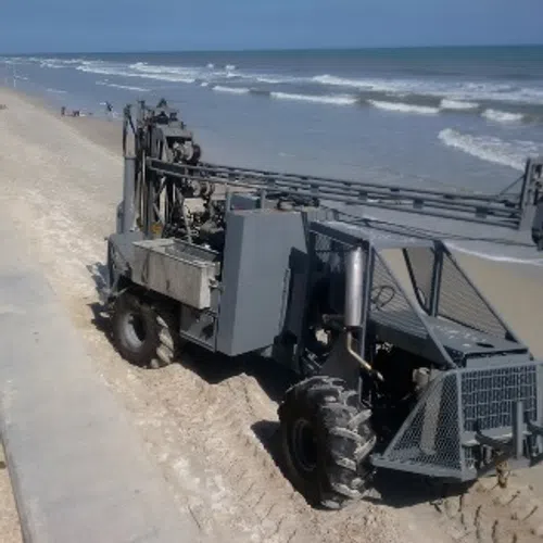 Heavy machinery working on a sandy beach near ocean waves under clear blue sky on a sunny day