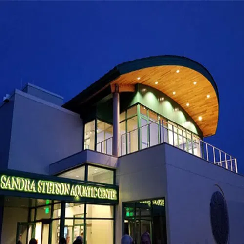 Modern Sandra Stetson Aquatic Center building lit up at night with curved wooden roof and glass windows.
