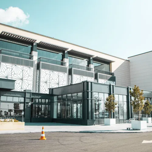 Modern commercial building with glass facade, palm trees, and geometric patterns on upper walls under clear sky.