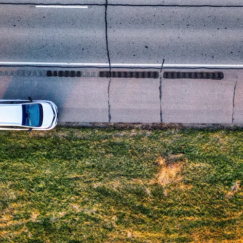 A white SUV parked on the side of a cracked asphalt road next to a grassy field at sunset.