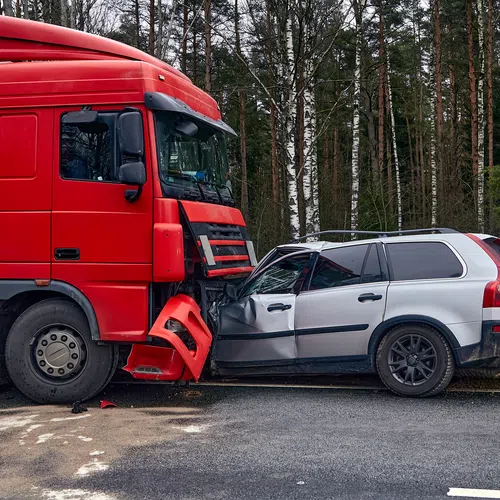 Red truck collided head-on with silver station wagon on roadside near forested area causing front-end damage.
