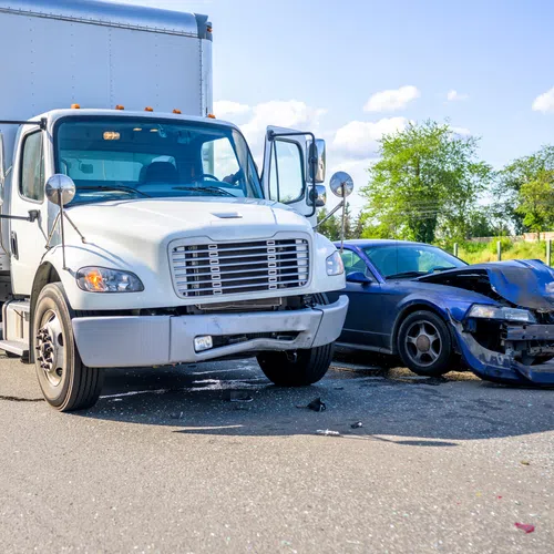 White delivery truck and damaged blue car after collision on road under clear sky