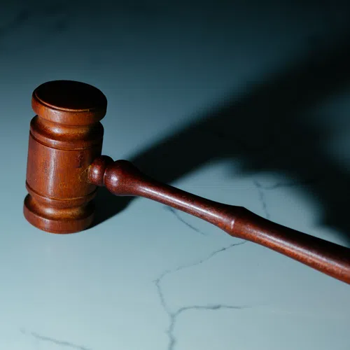 Wooden judge's gavel casting a shadow on a marble surface symbolizing law and justice.