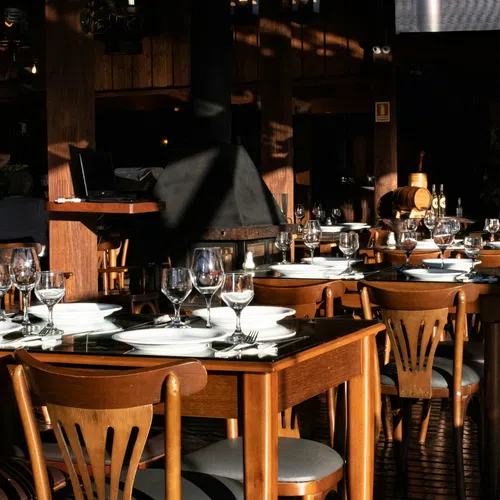 Sunlit restaurant interior with wooden tables set with white plates and multiple wine glasses.