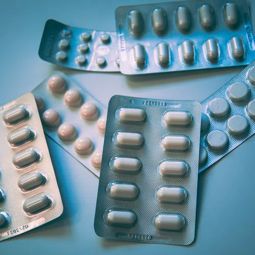 Several blister packs of white capsules and round tablets scattered on a flat surface with blue lighting.