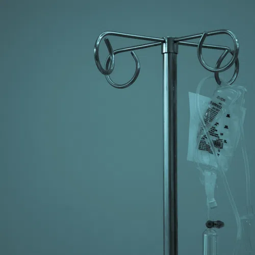 Metal IV stand holding a transparent intravenous fluid bag with tubing against a blue background.