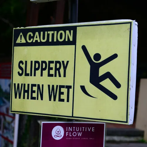Yellow caution sign warning slippery when wet with a falling person icon outdoors.