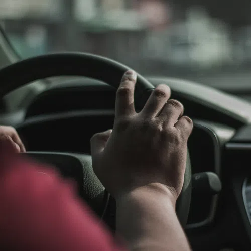 Close-up of hands gripping a steering wheel inside a car with dashboard and touchscreen visible.
