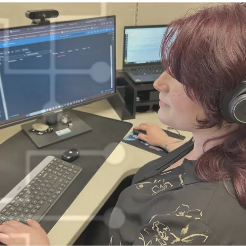 Person wearing headphones working on multiple screens with code and documents at a computer desk