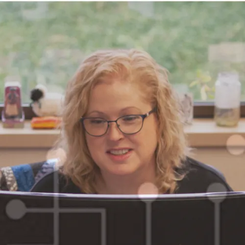 Woman with glasses working on a ViewSonic monitor in a bright room with plants and window view.