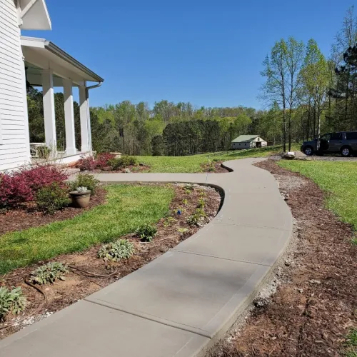a driveway with a white building and grass and trees
